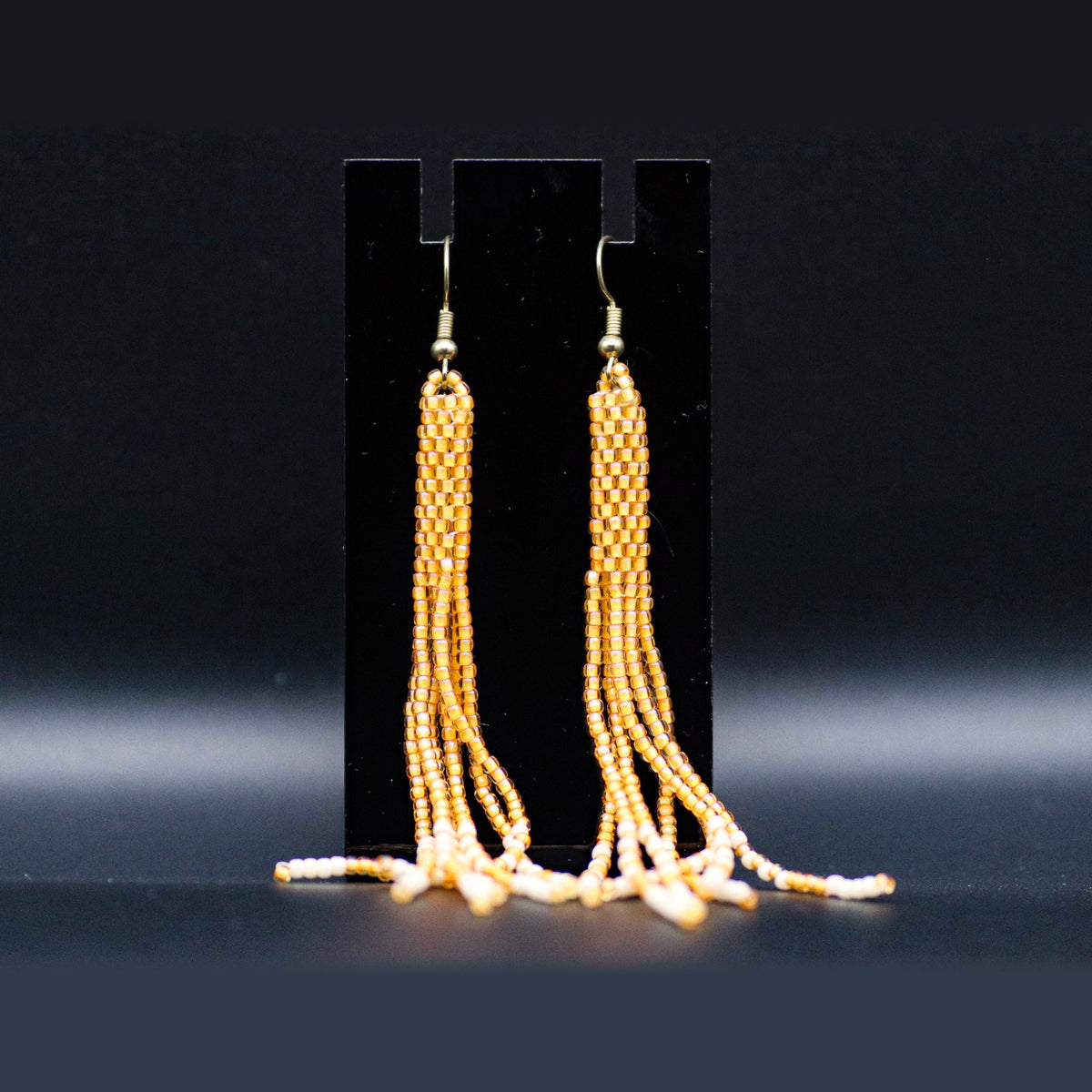 Gold and cream fringe earrings on a black stand, second view