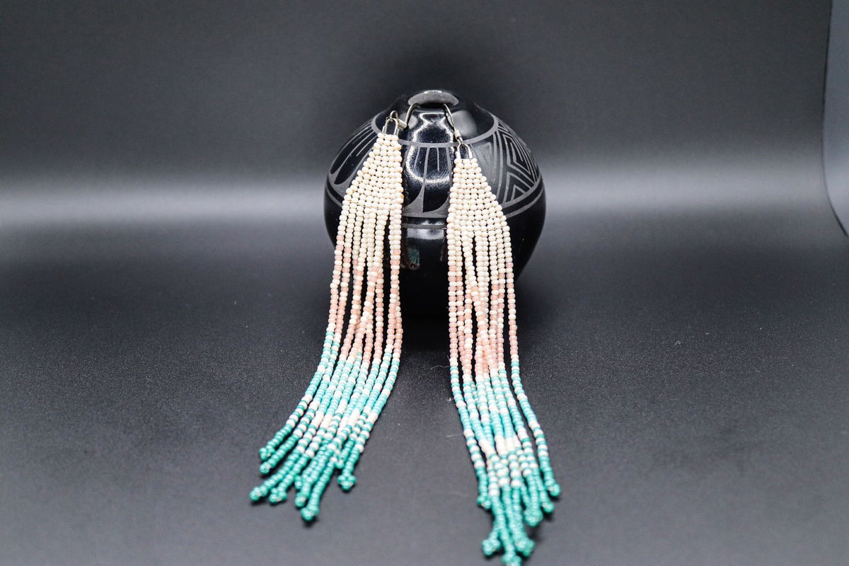 Long beaded fringe earrings in cream, blush and turquoise, displayed on black Diné pottery
